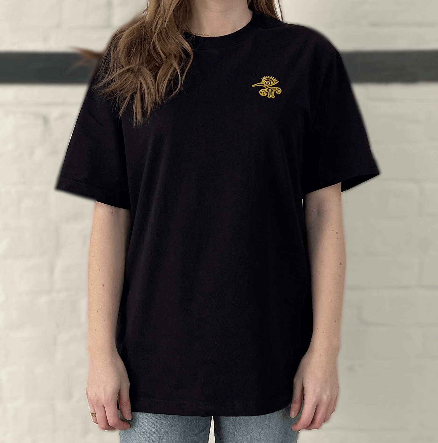 Schwarzes T-Shirt mit goldenem Mio Mio Tukan eingestickt auf der linken Brust