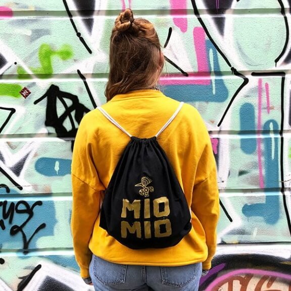 Frau trägt Schwarzen Mio Mio Baumwollbeutel mit goldenem Logo