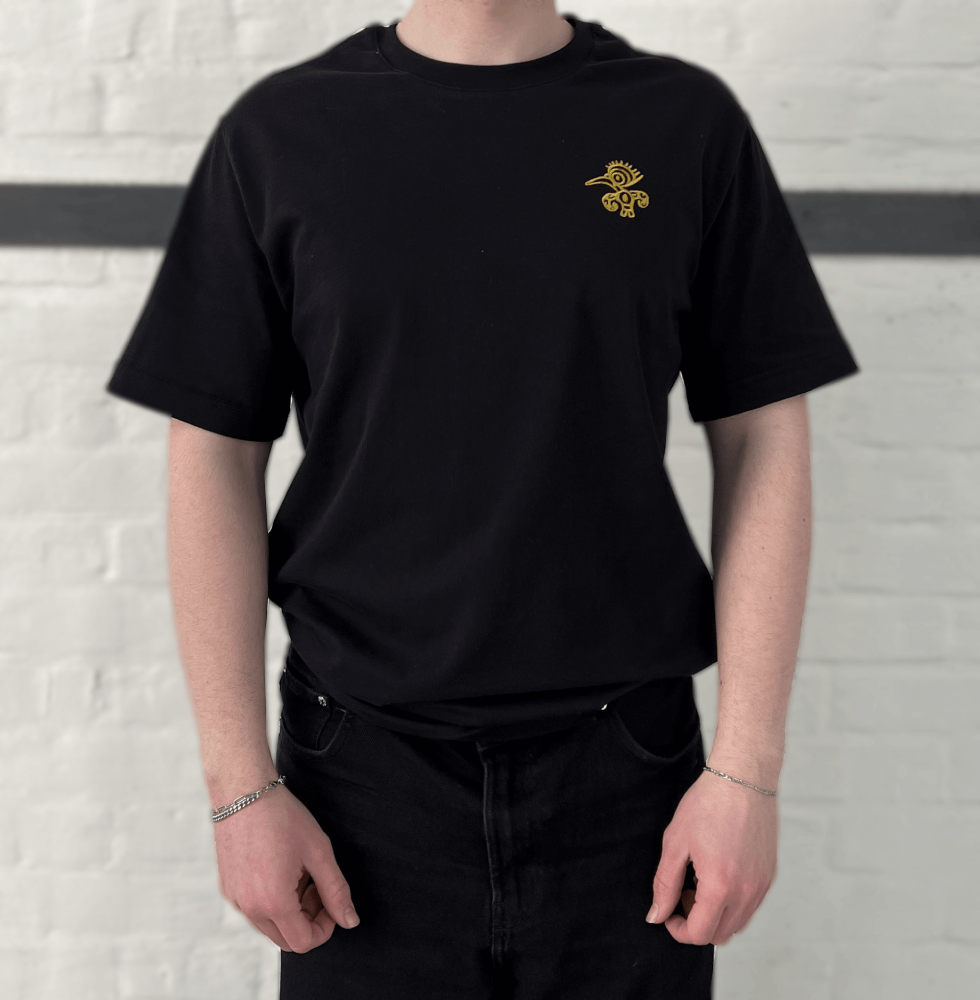 Schwarzes T-Shirt mit goldenem Mio Mio Tukan eingestickt auf der linken Brust